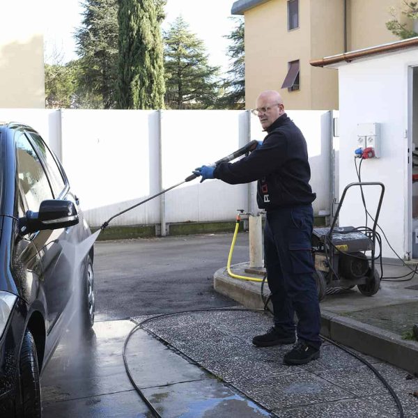 Pulitore professionale che lava un'auto con attrezzature specializzate.